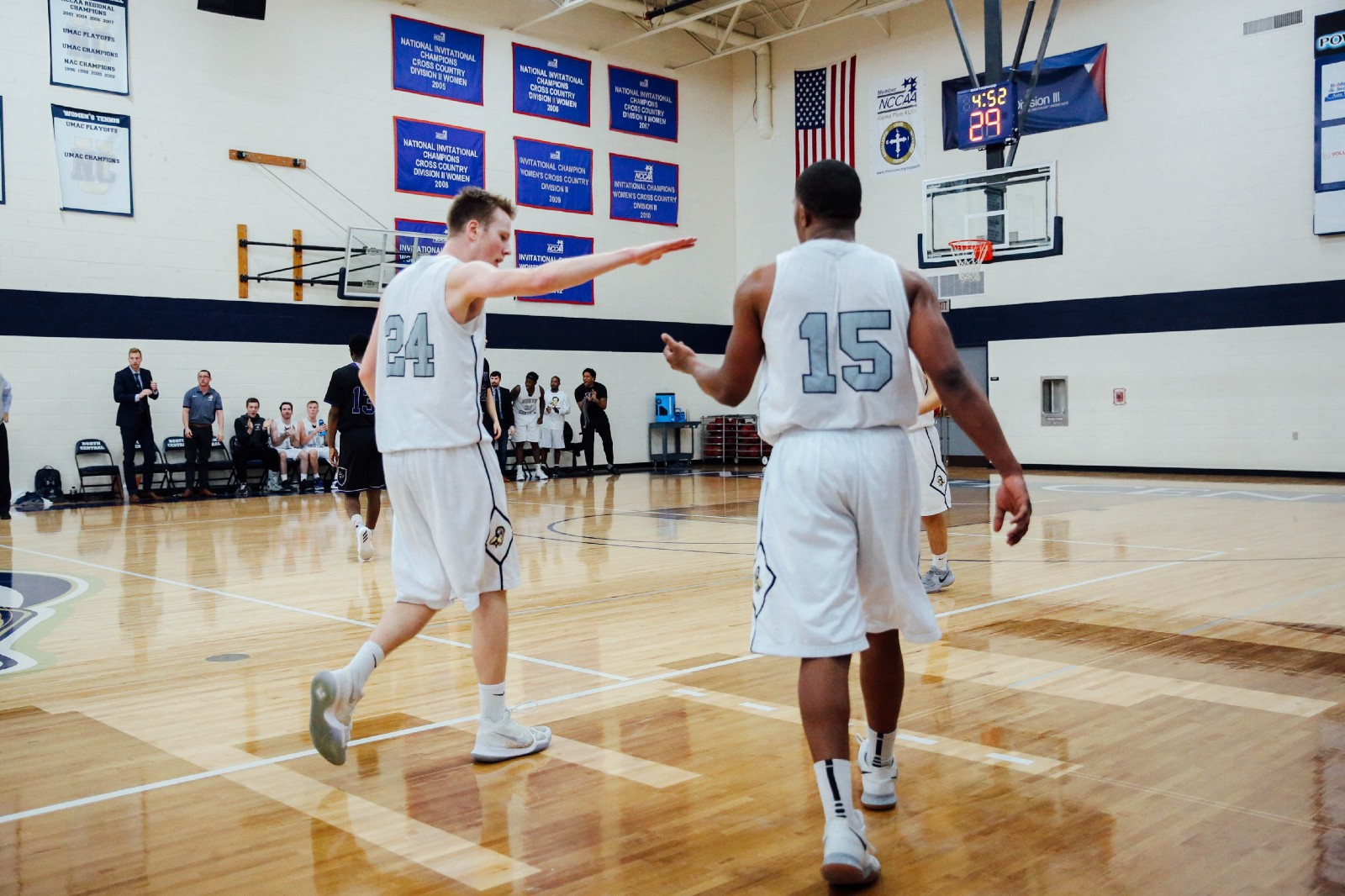 Two basketball teammates high fiving in an indoor basketball court wearing white uniforms.